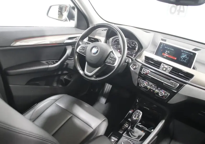 Vue intérieure côté conducteur du BMW X1 sDRIVE 18D 2019 avec tableau de bord moderne et sellerie cuir noire.