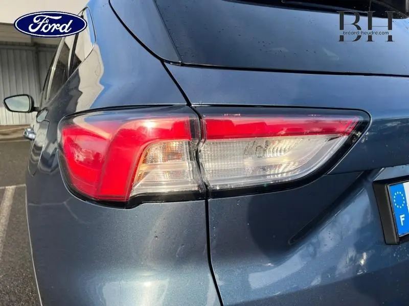 Gros plan sur le feu arrière droit d’un Ford Kuga bleu azur métallisé, avec partie de la carrosserie et plaque d’immatriculation visible.