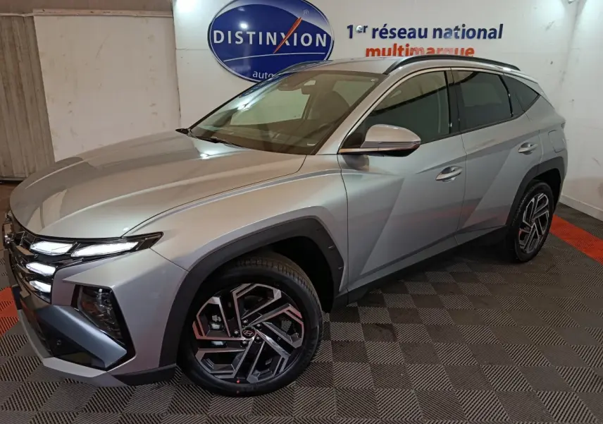 Vue 3/4 avant droit d'un Hyundai Tucson gris clair 2025 avec jantes alliage et calandre distinctive.