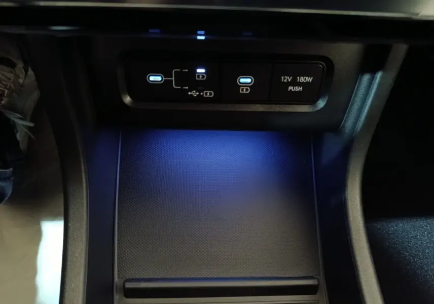 Gros plan sur la zone de recharge et ports USB éclairés en bleu dans l'habitacle du Hyundai Tucson gris clair 2025.