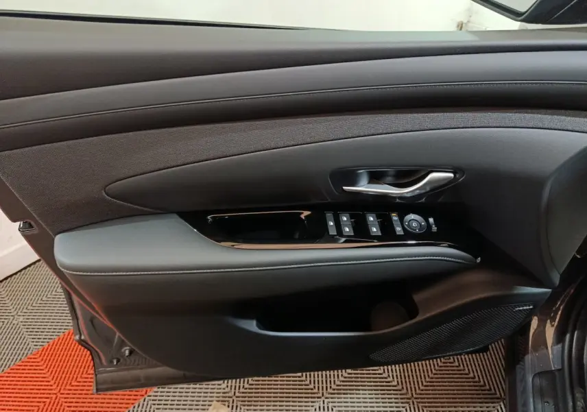 Vue intérieure côté gauche de la porte avant gris clair du Hyundai Tucson 2025 avec commandes de vitres et poignée argentée.