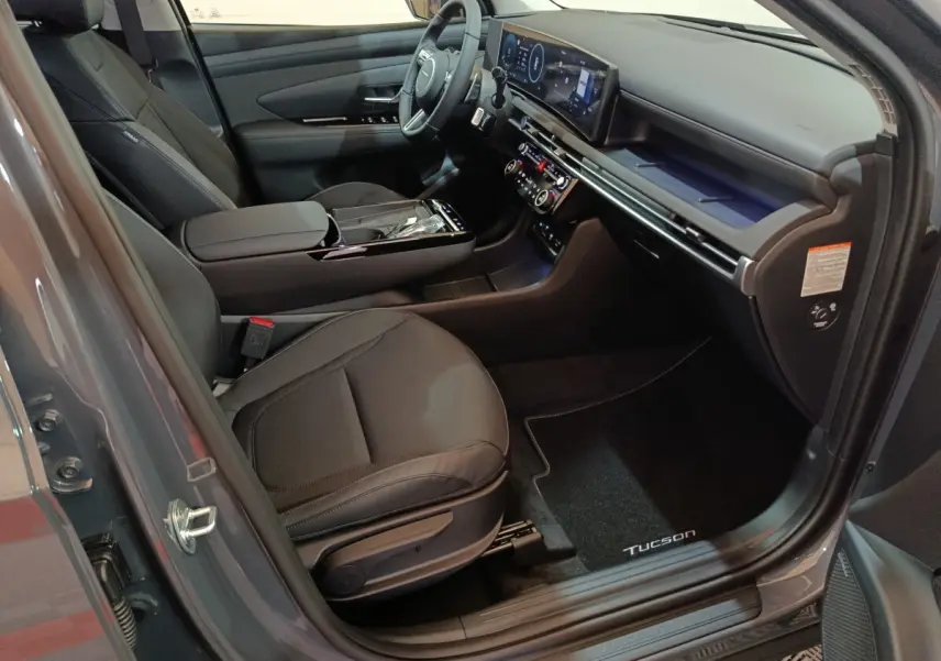 Vue intérieure côté conducteur du Hyundai Tucson 2025 gris clair, avec tableau de bord numérique et sièges noirs.