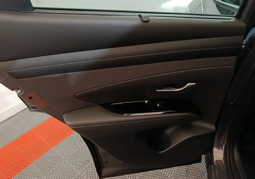 Vue intérieure côté gauche de la porte arrière du Hyundai Tucson 2025, avec garniture noire et poignée argentée.