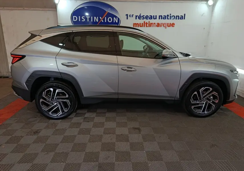 Vue latérale droite du Hyundai Tucson 1.6 Hybrid gris clair 2025, avec jantes alliage et toit noir contrasté.