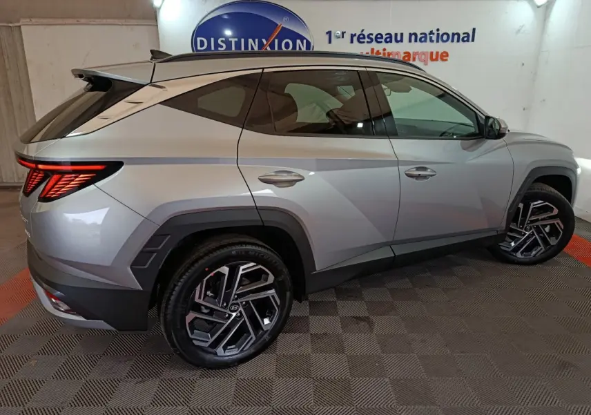 Vue latérale droite d'un Hyundai Tucson gris clair 2025 avec jantes noires et feux arrière LED allumés.