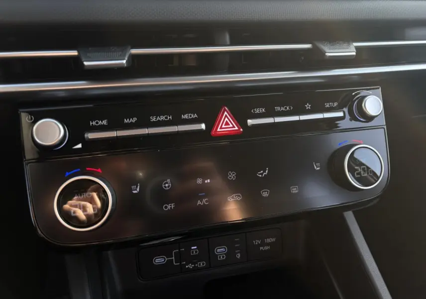Gros plan sur la console centrale du Hyundai Tucson 2025, avec commandes climatisation et multimédia noires brillantes.