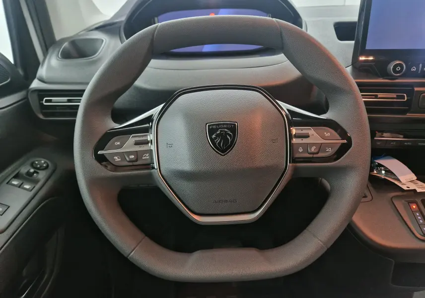 Vue rapprochée du volant noir du Peugeot Partner 2025 avec commandes intégrées et tableau de bord numérique.