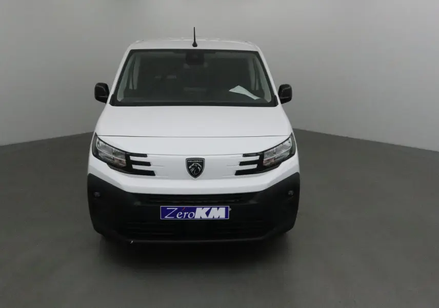 Vue frontale d'un Peugeot Partner blanc avec calandre noire et plaque "Zero KM" dans un espace neutre.