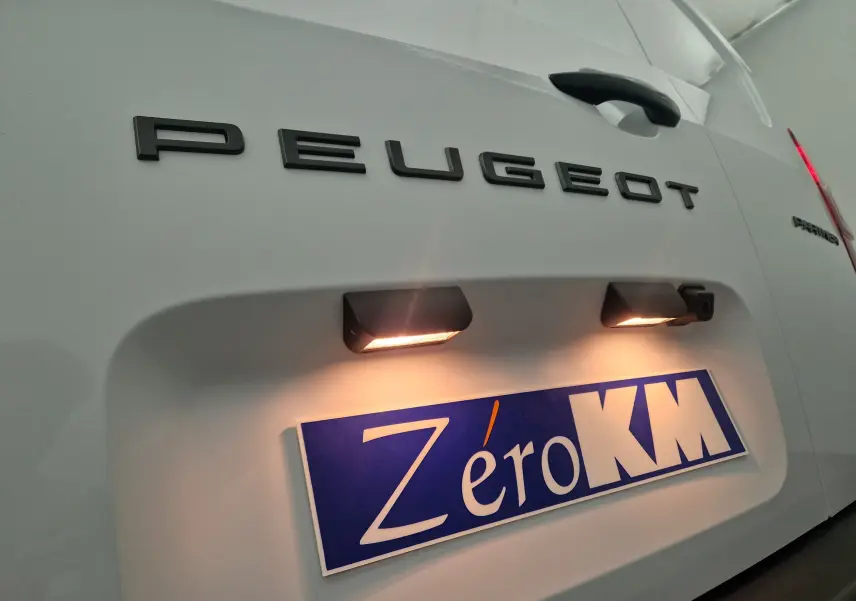 Gros plan sur l'arrière blanc du Peugeot Partner avec éclairage plaque et logo noir Peugeot bien visible.