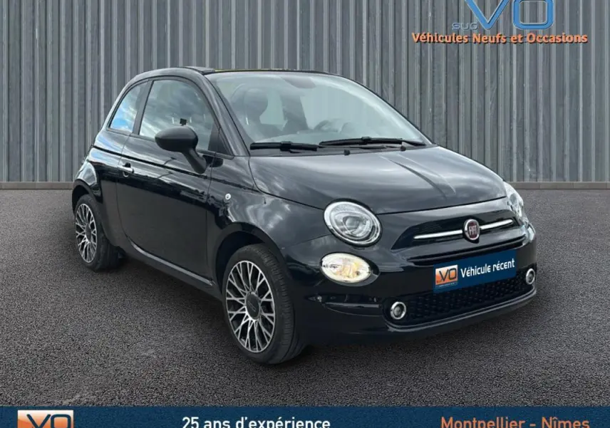 Vue 3/4 avant gauche d'une Fiat 500C noire 2024 avec jantes spécifiques et roue de secours visible sur le côté.