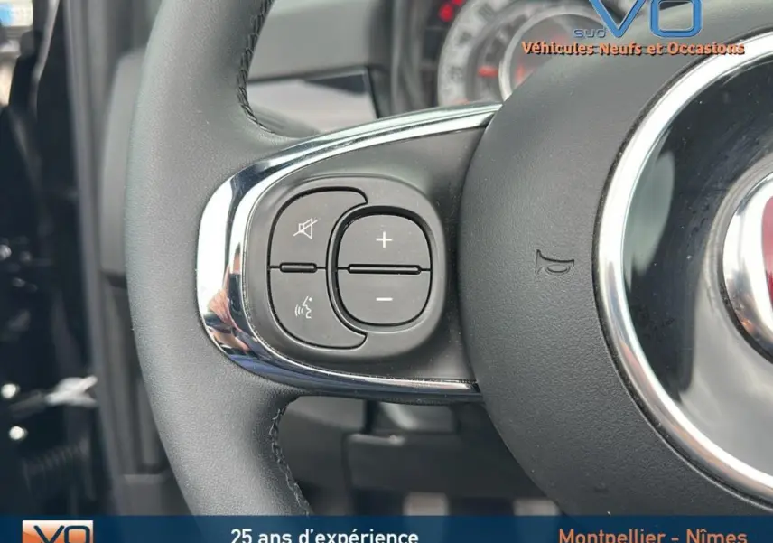 Gros plan sur les commandes au volant côté gauche du Fiat 500C noir 2024 avec volant en cuir et détails chromés.