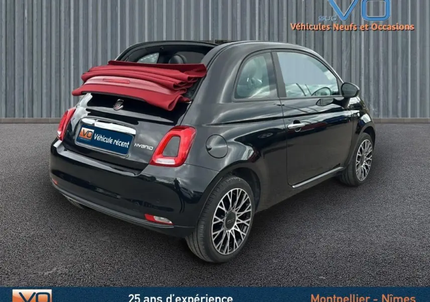 Vue 3/4 arrière droite d'une Fiat 500C noire 2024 avec toit rouge décapoté et roue de secours visible.