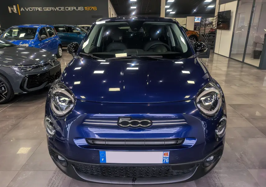 Vue avant d'un FIAT 500X bleu Venezia 2024 en showroom, avec logo 500 centré et phares ronds LED allumés.