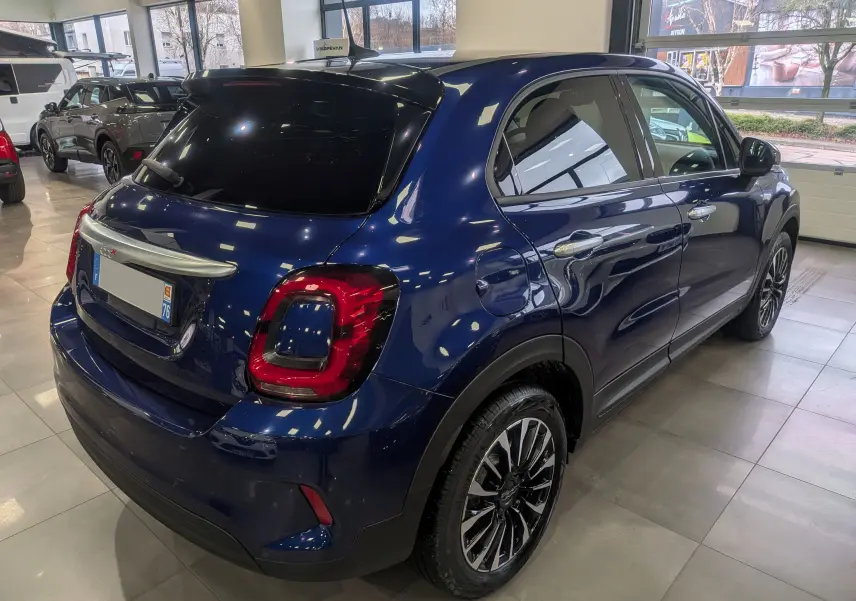 Vue 3/4 arrière droite d'une FIAT 500X bleu Venezia avec toit noir et jantes alliage en concession.