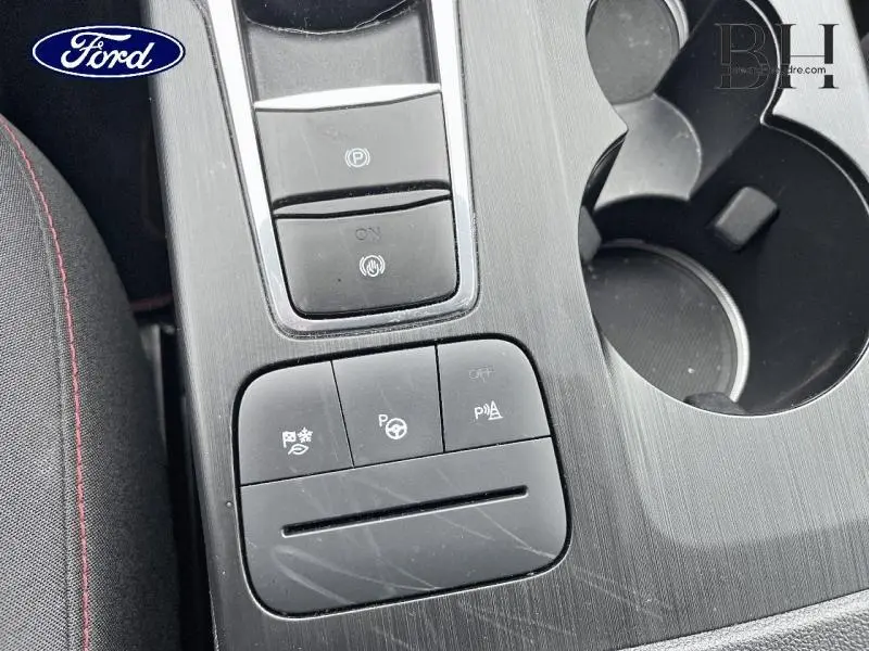 Gros plan sur la console centrale noire du Ford Kuga 2023 avec boutons d'assistance et porte-gobelets visibles.