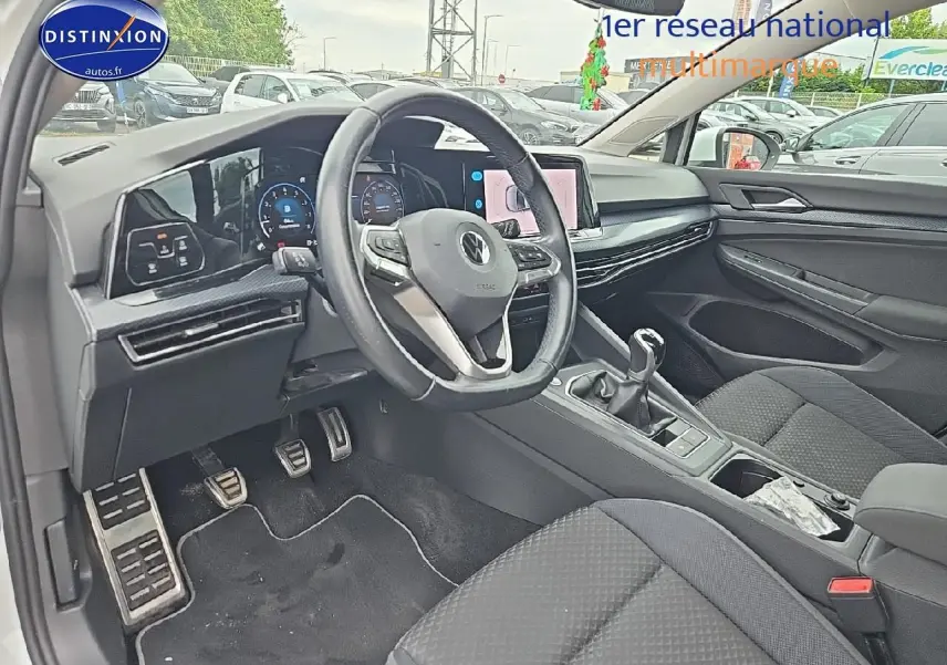 Vue intérieure côté conducteur de la Volkswagen Golf blanche, avec volant cuir multifonction et écran tactile central.