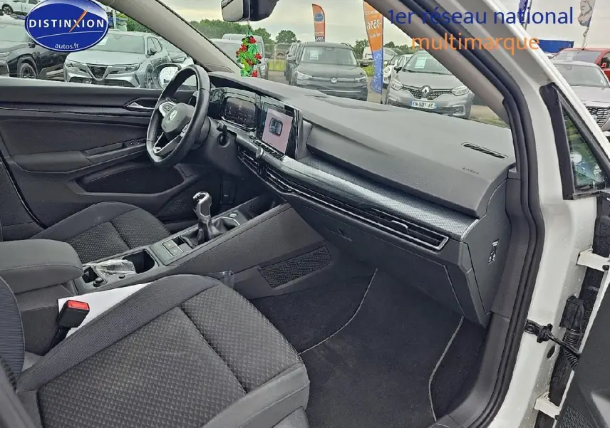 Vue intérieure côté passager d'une Volkswagen Golf blanche 2021 avec tableau de bord moderne et boîte manuelle.