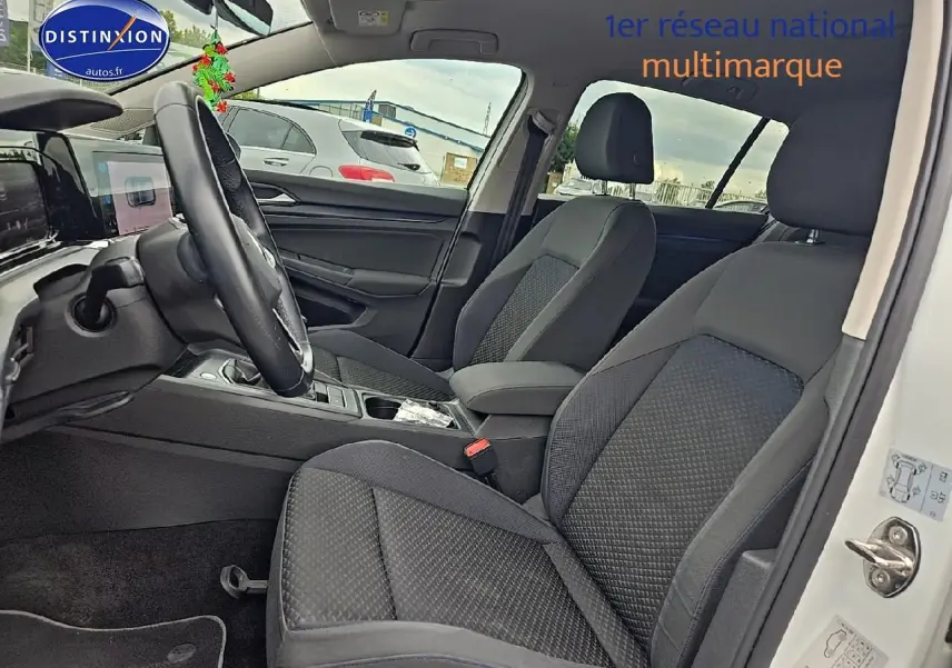 Vue intérieure côté conducteur de la Volkswagen Golf blanche 2021, sièges tissu gris et volant cuir multifonction.
