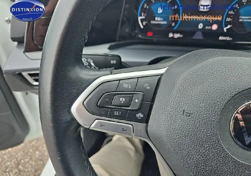 Gros plan sur le volant cuir multifonction noir de la Volkswagen Golf blanche, avec commandes de régulateur de vitesse visibles.