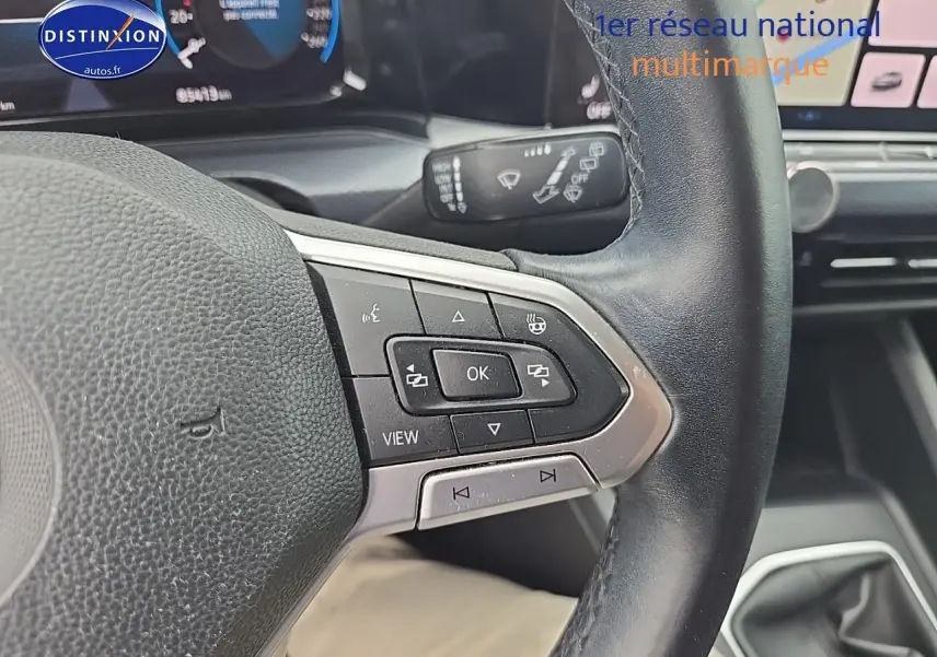 Gros plan sur le volant cuir noir multifonction côté gauche de la Volkswagen Golf blanche avec tableau de bord digital visible.