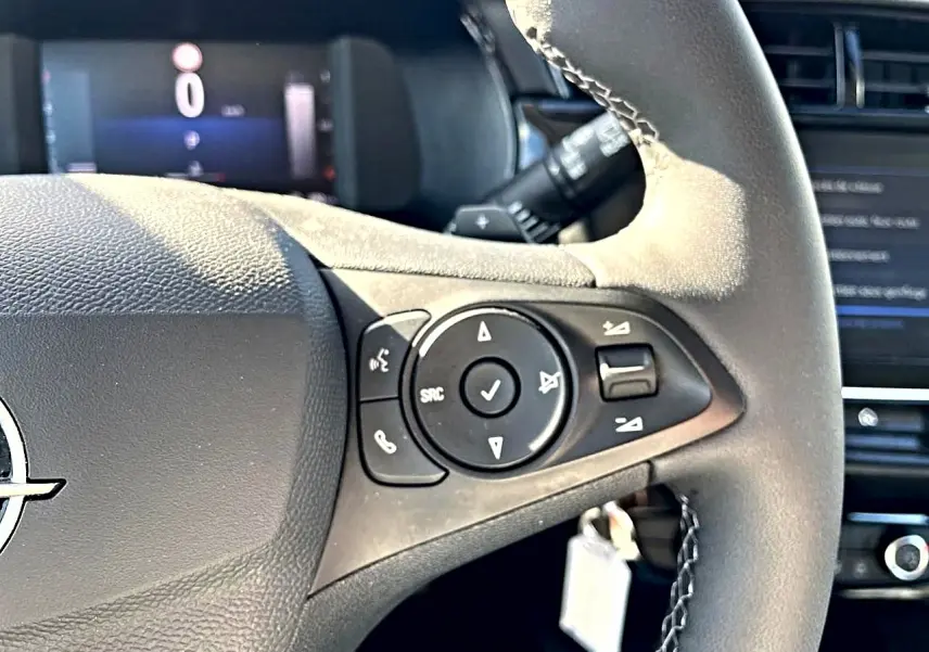 Gros plan sur le volant multifonction noir de l'Opel Corsa 1.2 turbo 100 edition, avec commandes audio visibles.