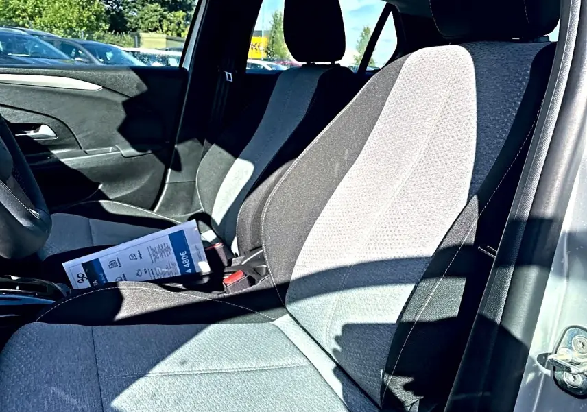 Vue intérieure côté conducteur de l’Opel Corsa gris 2025, sièges tissu bicolore noir et gris avec brochure posée dessus.
