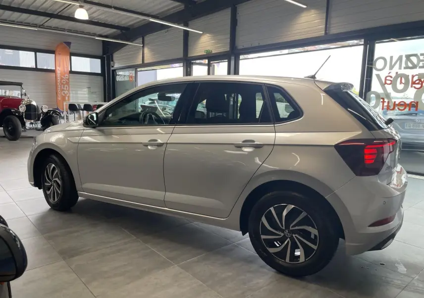Volkswagen Polo gris clair vue de profil côté gauche en intérieur avec jantes alliage et vitres teintées.