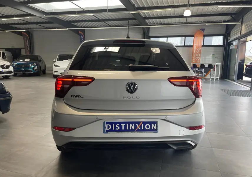 Vue arrière d'une Volkswagen Polo gris clair 2024 avec feux LED et lunette arrière surteintée en showroom.