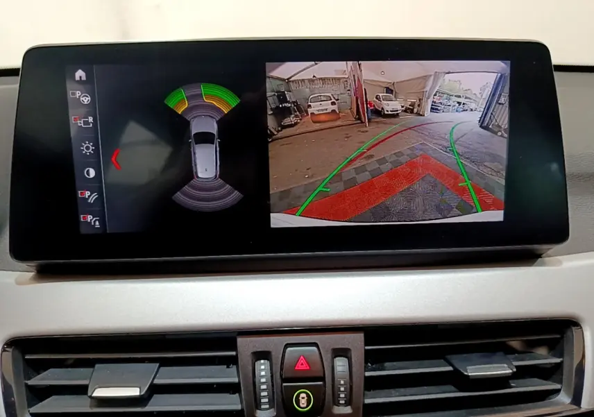 Écran multimédia montrant la caméra de recul et les capteurs de stationnement du BMW X1 blanc, vue intérieure.