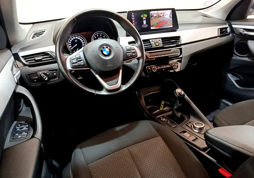 Vue intérieure avant de la BMW X1 sDrive18i Lounge 2019, volant cuir, écran multifonctions et levier de vitesses manuel.