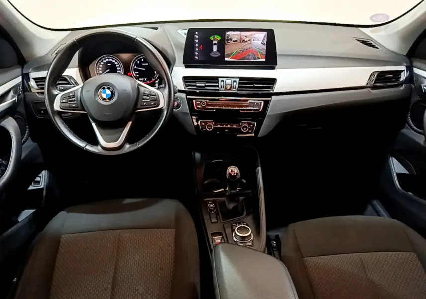 Vue intérieure avant du BMW X1 sDrive18i Lounge 2019, tableau de bord noir avec écran multimédia et volant cuir multifonctions.