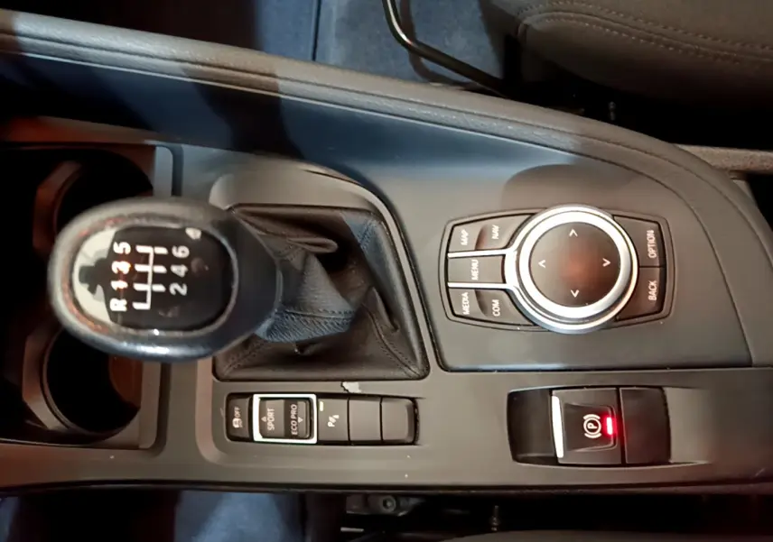 Vue plongeante sur la console centrale noire du BMW X1 sDrive18i 2019 avec levier de vitesse manuel et molette de contrôle.