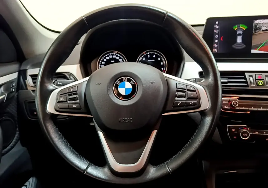 Vue rapprochée du volant cuir noir multifonctions et du tableau de bord digital d'une BMW X1 sDrive18i Lounge 2019.