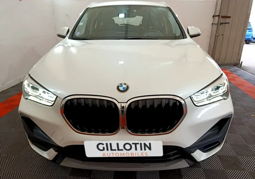 Vue frontale d'un BMW X1 sDrive18i Lounge blanc avec phares LED allumés et calandre noire distinctive.