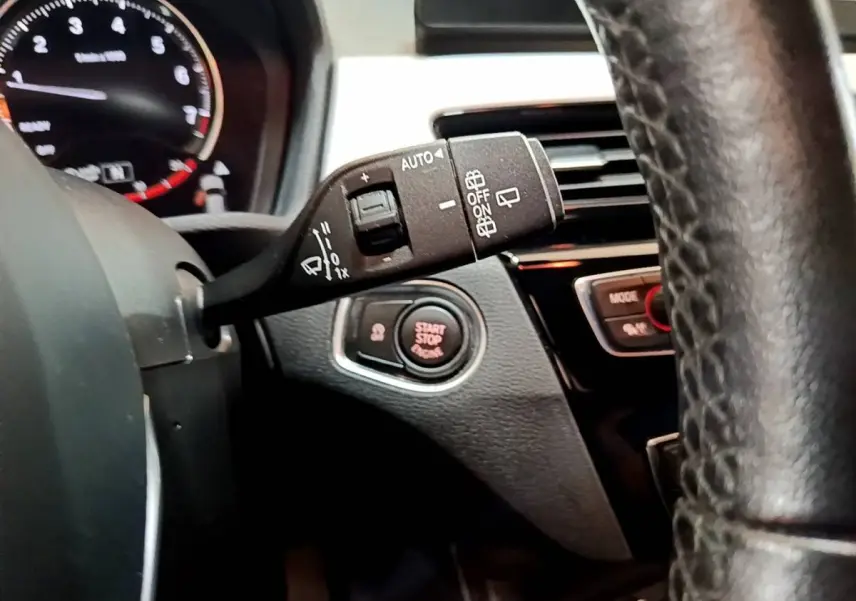 Gros plan sur la manette d’essuie-glace et le bouton start/stop du tableau de bord d’une BMW X1 blanche, intérieur noir.