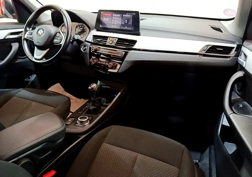 Intérieur avant droit de BMW X1 sDrive18i 2019, tableau de bord noir avec écran central et levier de vitesse manuel.