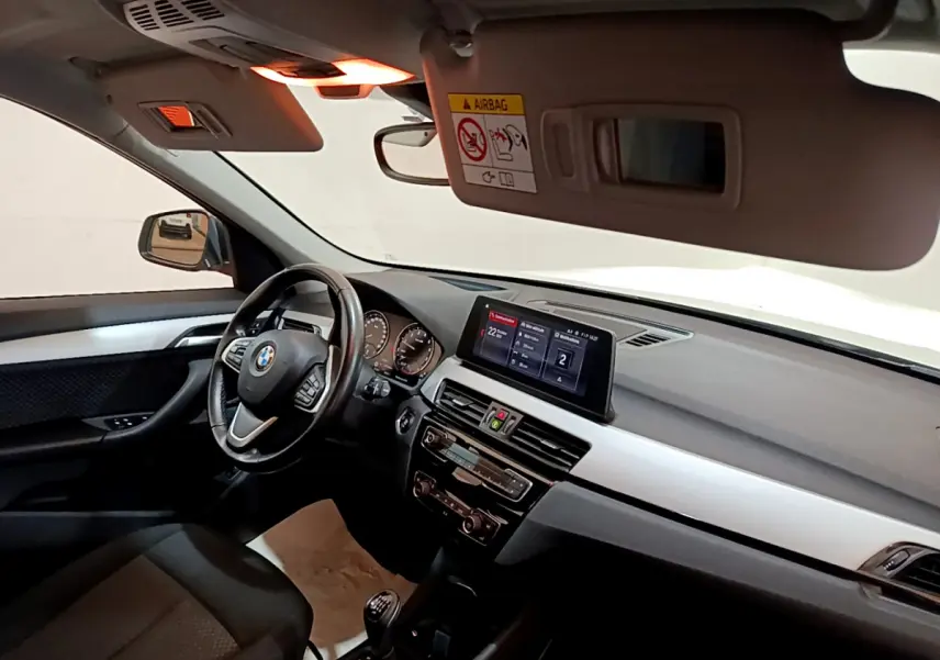 Vue intérieure côté conducteur du BMW X1 blanc 2019, volant cuir multifonctions et écran central 6,5 pouces.