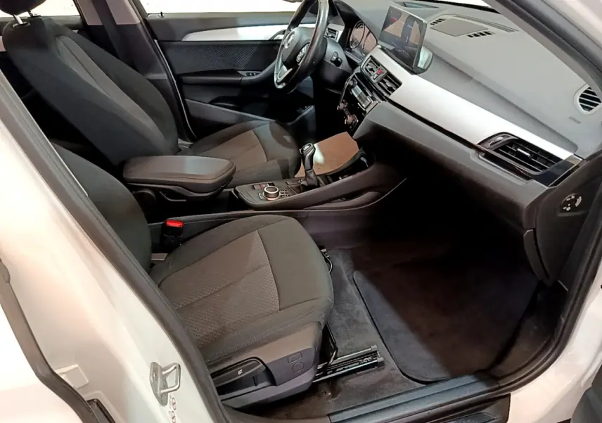Vue intérieure côté conducteur de la BMW X1 sDrive18i Lounge 2019, sièges noirs et tableau de bord moderne.