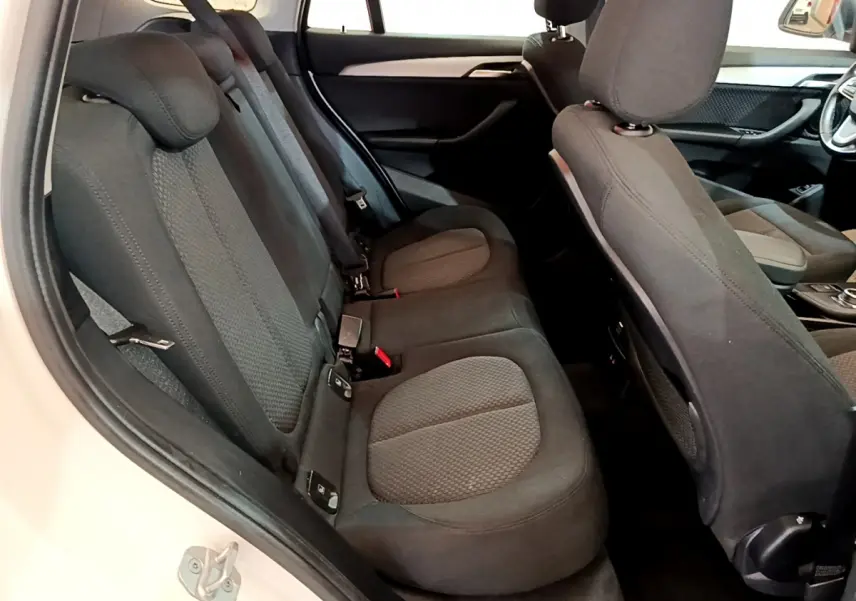 Vue intérieure côté gauche sur les sièges arrière noirs et le dossier avant du BMW X1 sDrive18i Lounge blanc.
