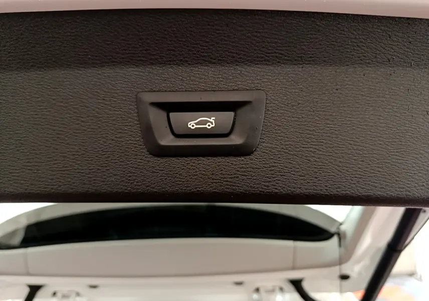 Bouton d'ouverture électrique du coffre sur la partie intérieure du hayon arrière blanc d'un BMW X1 sDrive18i Lounge.