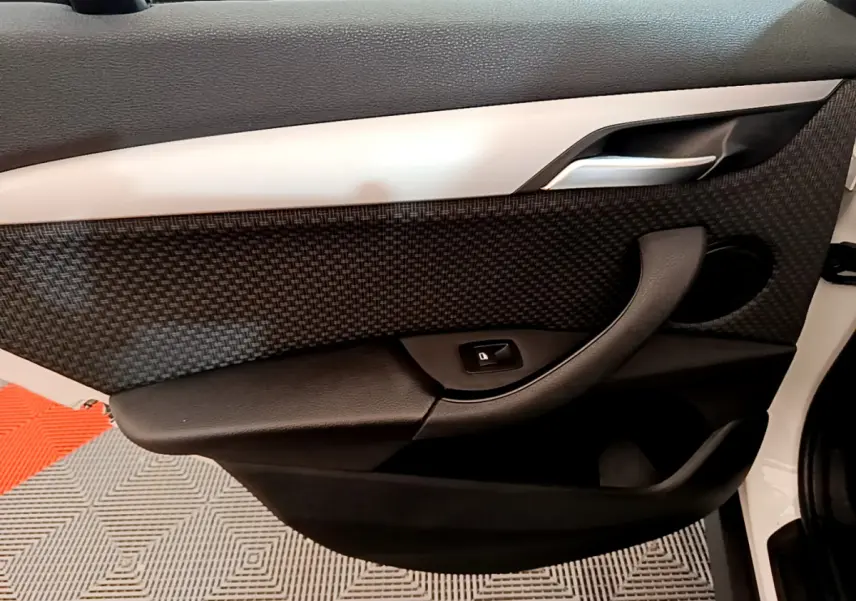 Vue intérieure du panneau de porte avant droit du BMW X1 sDrive18i Lounge blanc, avec insert texturé et commande de lève-vitre.