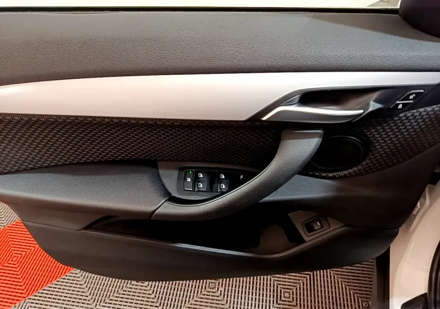 Vue intérieure du panneau de porte côté conducteur du BMW X1 blanc, avec commandes de vitres et poignée argentée.