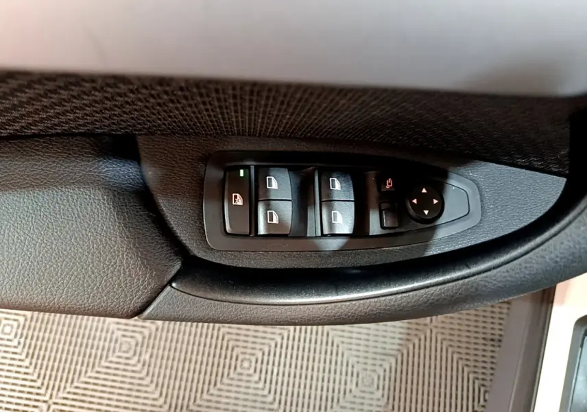 Gros plan sur les commandes de lève-vitres et rétroviseurs côté conducteur du BMW X1 blanc sDrive18i Lounge 2019.