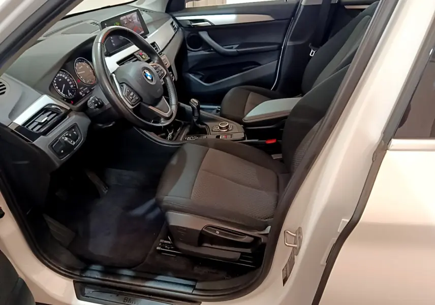 Intérieur côté conducteur d'une BMW X1 sDrive18i blanche, montrant le volant cuir et la boîte manuelle.