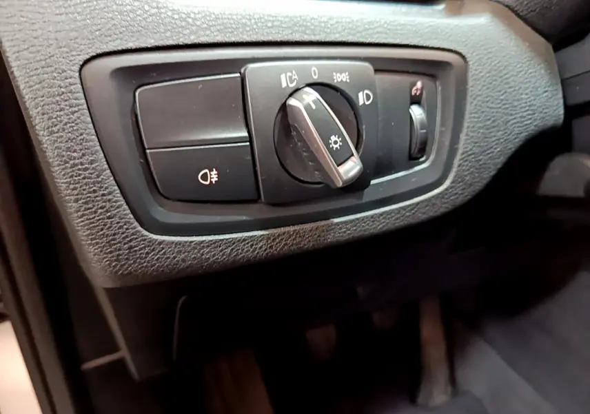 Gros plan sur le bouton de commande des phares noir dans l'habitacle du BMW X1 sDrive18i Lounge blanc.