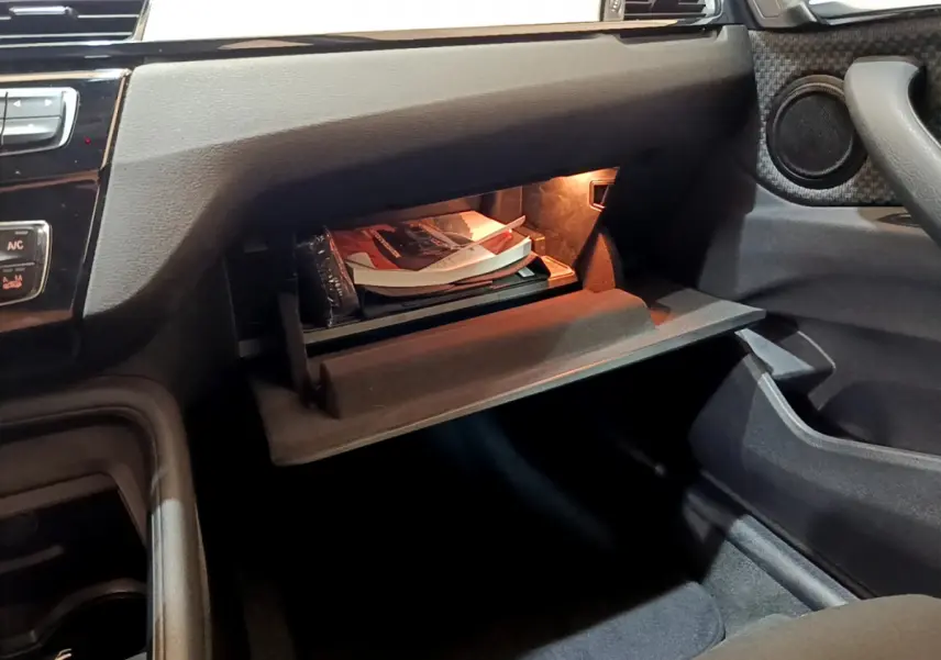 Gros plan sur la boîte à gants ouverte côté passager de la BMW X1 sDrive18i Lounge 2019 avec éclairage intérieur.