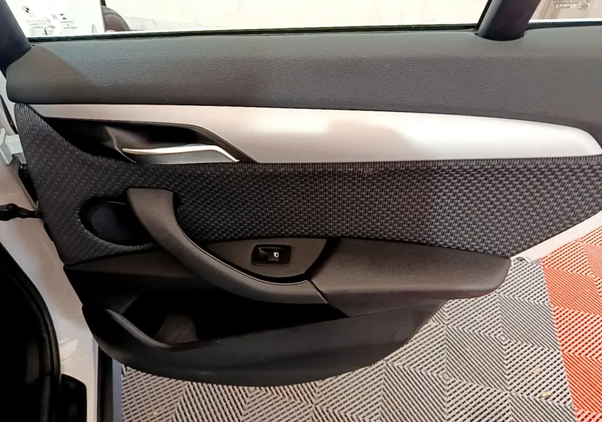 Vue intérieure côté gauche de la porte avant d’un BMW X1 sDrive18i Lounge blanc avec garniture tissu et plastique noir.