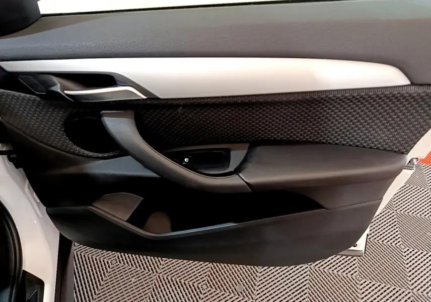 Détail de la porte avant gauche de la BMW X1 sDrive18i Lounge blanche, avec garniture noire texturée et poignée intégrée.