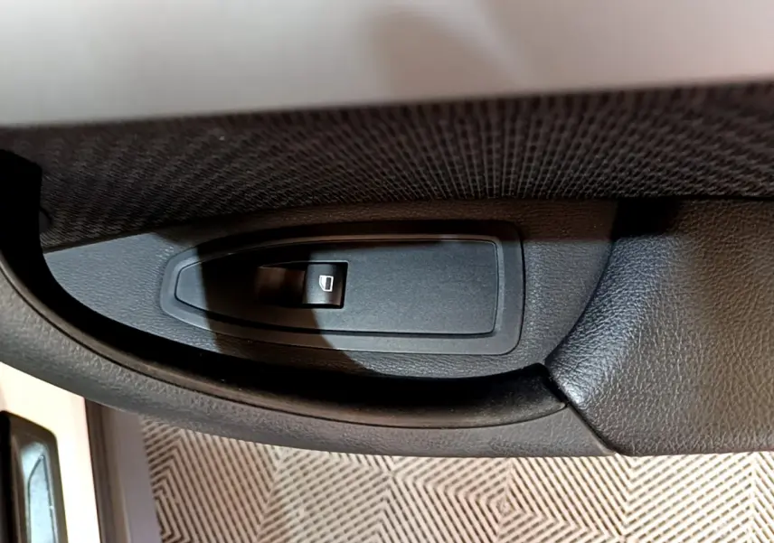 Gros plan sur le bouton de lève-vitre électrique côté conducteur d'une BMW X1 sDrive18i Lounge blanche.