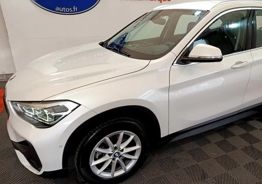 Vue 3/4 avant droit d'un BMW X1 sDrive18i Lounge blanc avec jantes alliage et rétroviseurs blancs.